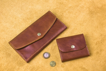 two brown stitched purses of different sizes and shapes with coins on a yellow background