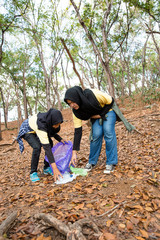 Two young woman hijab volunteers cleaning rubbish from park together