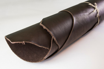 roll of dark brown leather tied with a beech rope close up on a white background