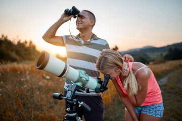 Young man and woman looking at the sky with a telescope and binoculars.