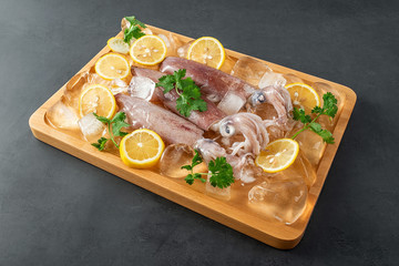 A plate of ice cubes with fresh tubules of squid and lemon slices on a black background