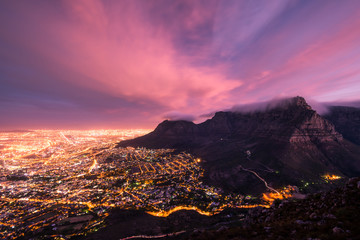 Naklejka premium Moody Table Mountain after sunset with city lights as seen from Lions Head.