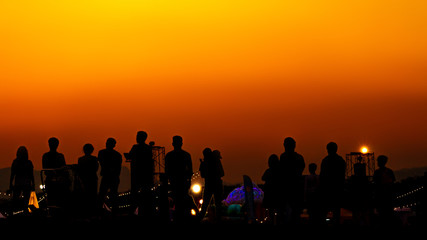 Fototapeta na wymiar Silhouette of many tourists are taking pictures by smart phone on the top of the mountain during sunset times.