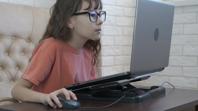 Surprised child is looking at the computer. A little girl in glasses gazes intently into a laptop monitor.