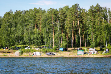 Fototapeta na wymiar Argazi, Russia - July, 2019: Camping with tents and cars on the shore of the lake. Illustration of environmental pollution and violations of the water protection zone.