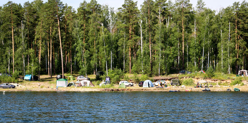 Argazi, Russia - July, 2019: Camping with tents and cars on the shore of the lake. Illustration of environmental pollution and violations of the water protection zone.
