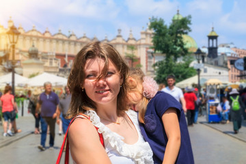 Fototapeta na wymiar beautiful girl holding tired daughter in main square of Krakow. concept of traveling with kids. Happy parents do not leave their children at home