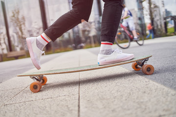 Picture of legs of woman in black jeans riding skateboard on street in city
