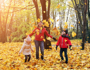 happy family walking in sunny park and throws orange maple leaves. mother with kids enjoying autumn weather outdoors