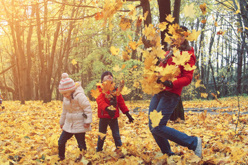 happy family walking in sunny park and throws orange maple leaves. mother with kids enjoying autumn weather outdoors