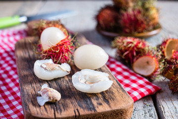 Mix of whole and peeled rambutan on wooden cutting board and table. Rambutan is an exotic fruits from tropical countries.