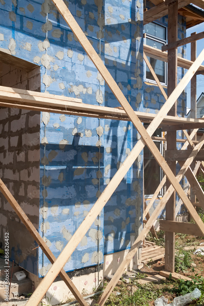 Poster facade of cottage under construction with building grid applied to walls and guides for plaster appl