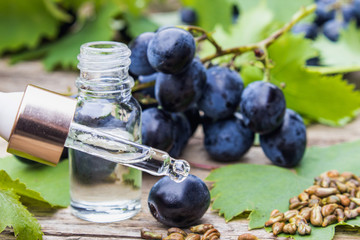 Grape seed oil in a glass jar and fresh grapes on old wooden boards. The concept of SPA, Eco products.