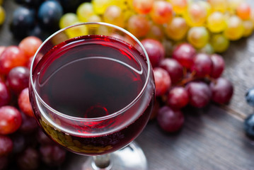 glass of red wine and grapes on black wooden table background