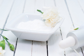 cosmetic cream and white carnation flowers on bright wooden table