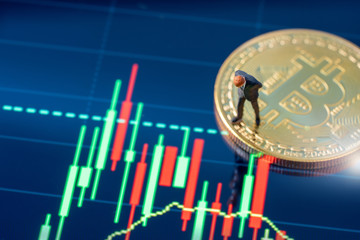 Miniature people business man standing on bitcoins coins and market trading data chart.