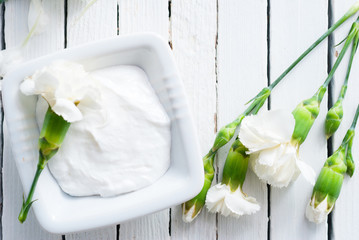 cosmetic cream and white carnation flowers on bright wooden table