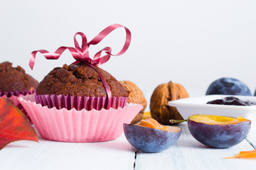 chocolate muffins and jelly, plums, walnuts on white wooden table