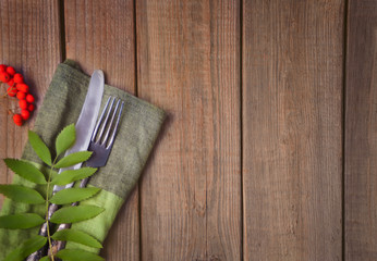 Fototapeta na wymiar Wooden table with cutlery, green napkin and rowan. Autumn harvest. Autumn concept. Table decoration. Top view. Copy space