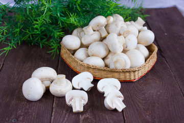 Champignon mushrooms in a wicker bowl on a dark background with a sprig of greenery