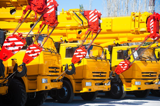 Mobile construction cranes with yellow telescopic arms and big tower cranes in sunny day