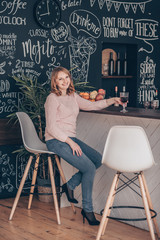 Fototapeta premium Young woman sitting on a chair near desk in the modern loft kitchen.