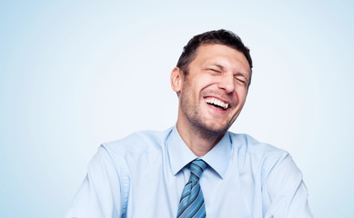 Portrait of a real happy laughing bearded man in a shirt with a tie on light blue background