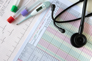 Blood tests,  a digital thermometer, and a stethoscope on top of a table