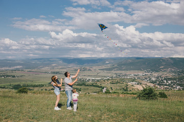 Happy family flying a colorful kite on green meadow.