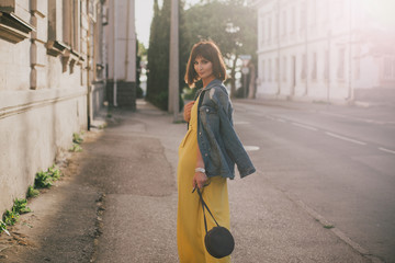 Woman in stylish yellow jumpsuit posing on city streets.
