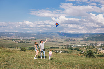 Happy family flying a colorful kite on green meadow.