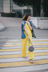 Beautiful woman in yellow jumpsuit posing on city streets.