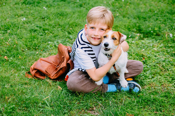 A sitting on the grass smiling boy is hugging his pet