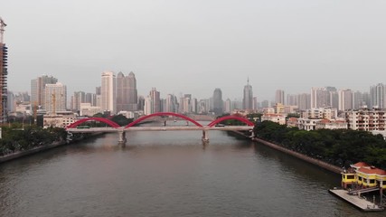 Aerial shot of Jiefang bridge spanning across Pearl river, green trees grow along banks, dense build central area of Guangzhou city. Camera slowly ascent, wide angle shot
