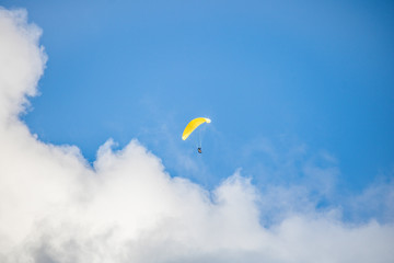 Paraglider floating through clouds and blue sky over Camps Bay, Cape Town.