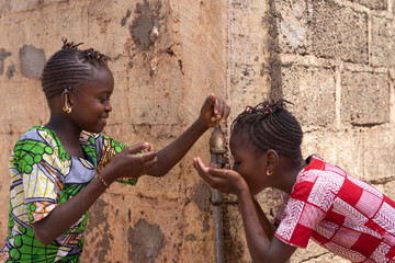 Two Girls Happily Sharing Water from tap in Bamako, Mali
