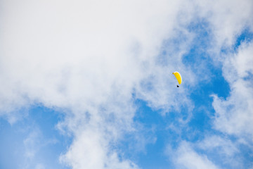 Paraglider floating through clouds and blue sky over Camps Bay, Cape Town.