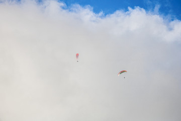 Two paragliders floating through clouds over Camps Bay, Cape Town.
