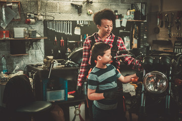 Fototapeta na wymiar African american woman mechanic and boy helper repairing a motorcycle in a workshop