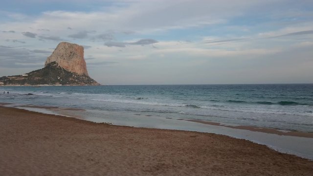 Beautiful view of Penyal d'Ifac and Costa Blanca wavy beach with cloudy blue sky on a calm spring afternoon