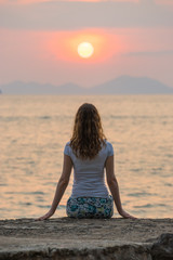 Fototapeta na wymiar One young woman sits on seashore and looks on beautiful scarlet sunset and seascape in Krabi. Back view.