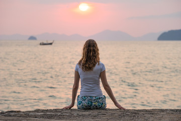 Fototapeta na wymiar Woman sits alone on seashore and looks on beautiful scarlet sunset and seascape in Krabi. Back view.