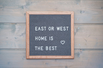 Grey lettering Board with felt coating in wooden frame with English text " East or West - home is the best" on the wall of wooden house