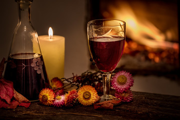 Cozy evening still life by . A glass of red wine, an old decanter, green leaves and dried flowers...