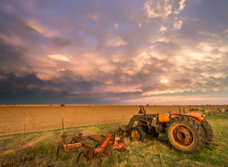 Old tractor and plow on rural farmlands during drought as a big rain storm moves in over the fields.