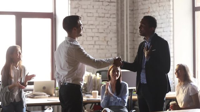 European young boss congratulating african male worker with promotion