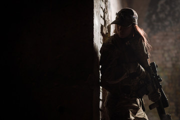 Silhouette of warrior girl with weapon in full ammunition in doorway. Conceptual military photo