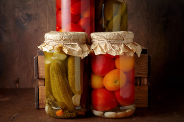 Homemade pickled tomato and cucumber in glass jars on an wooden rustic background