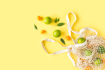 Mesh shopping bag with lyme on yellow background. Pattern made of summer tropical fruits. Food concept. Flat lay, top view