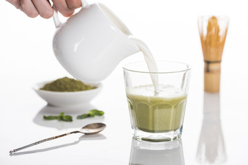 cropped view of woman pouring milk into matcha tea on table with whisk and tea powder